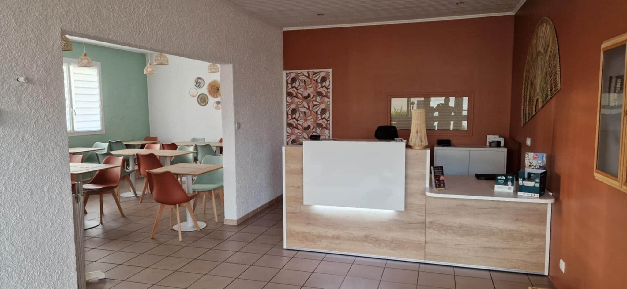 A dining area with tables and chairs, a reception desk, and a wall with decorative patterns.
