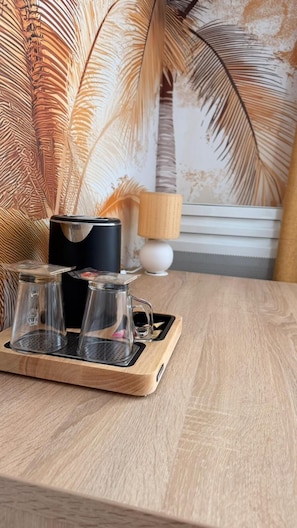 A wooden tray with two clear glass cups and a black container on a table.
