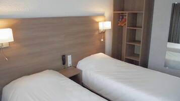 Ein Hotelzimmer mit zwei Betten, einem Holzkopfende, Nachttischlampen, einem kleinen Tisch und einem Kleiderschrank mit Kleidung.