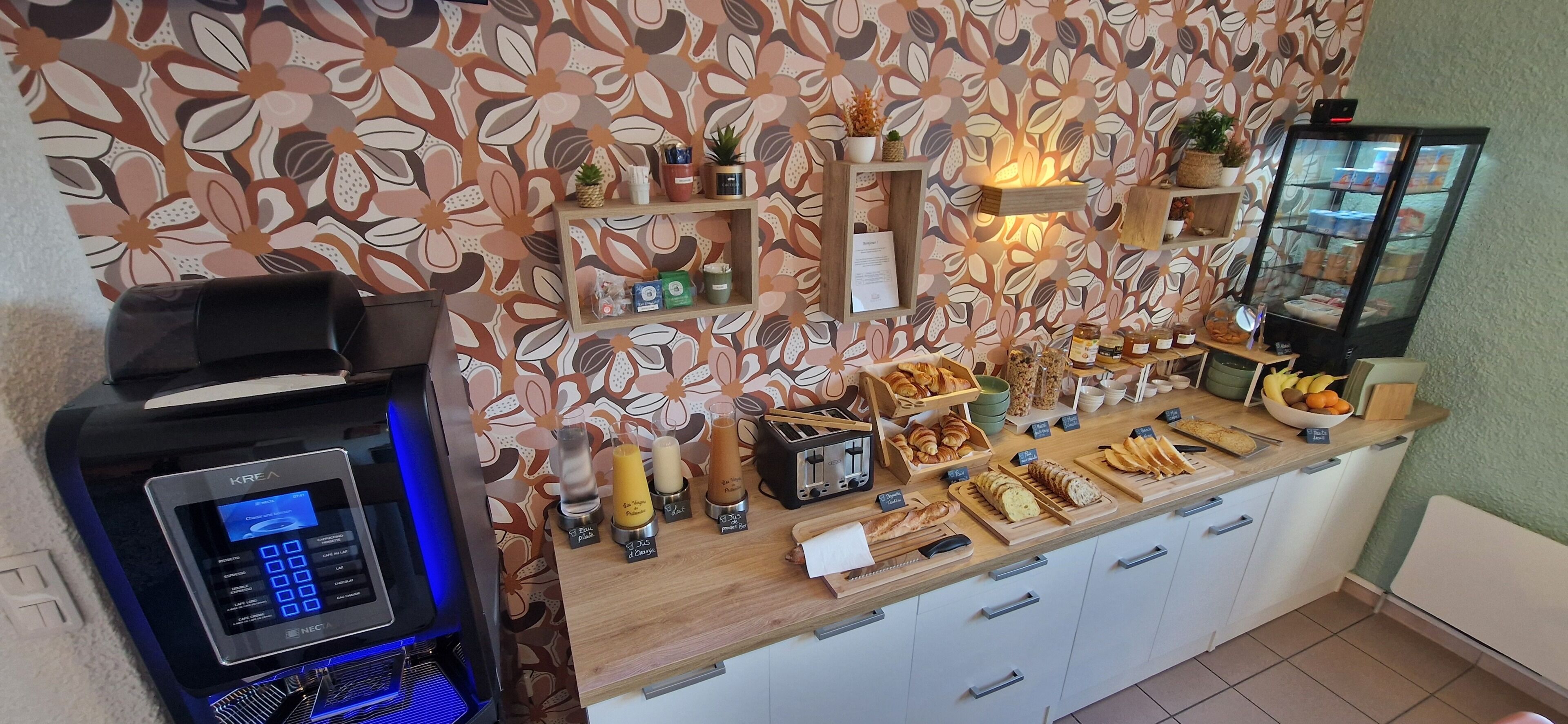 Una barra de desayuno con una máquina de café, diversas opciones de pastelería y una vitrina con alimentos.