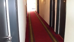 A hotel hallway with a red carpet, black doors, and wall-mounted lights.