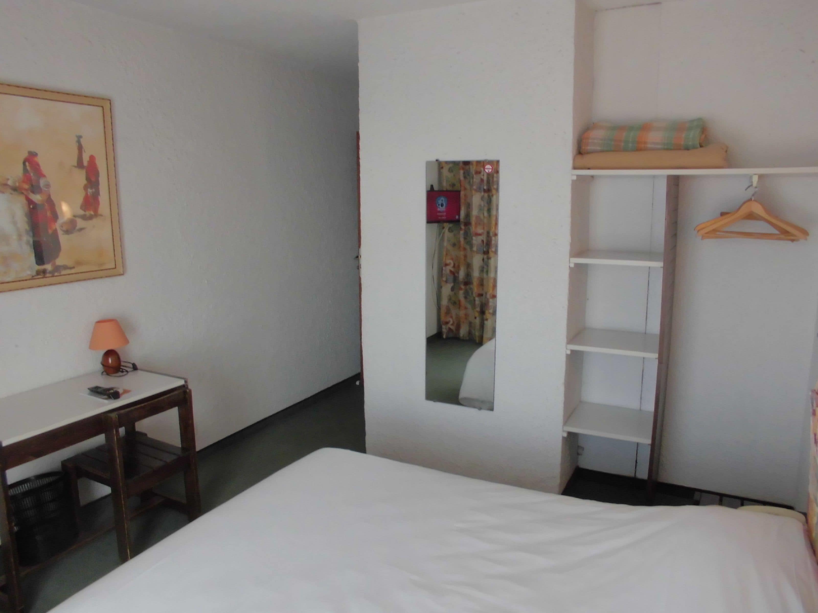Une chambre d’hôtel avec un lit, un bureau doté d’une lampe, une armoire et un tableau au mur.
