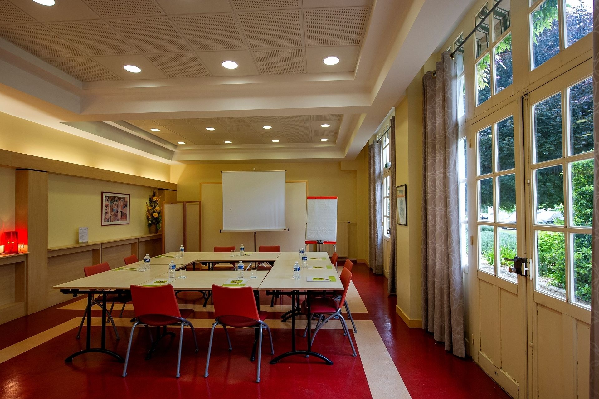 A conference room with a long table, red chairs, a whiteboard, and a projector screen.