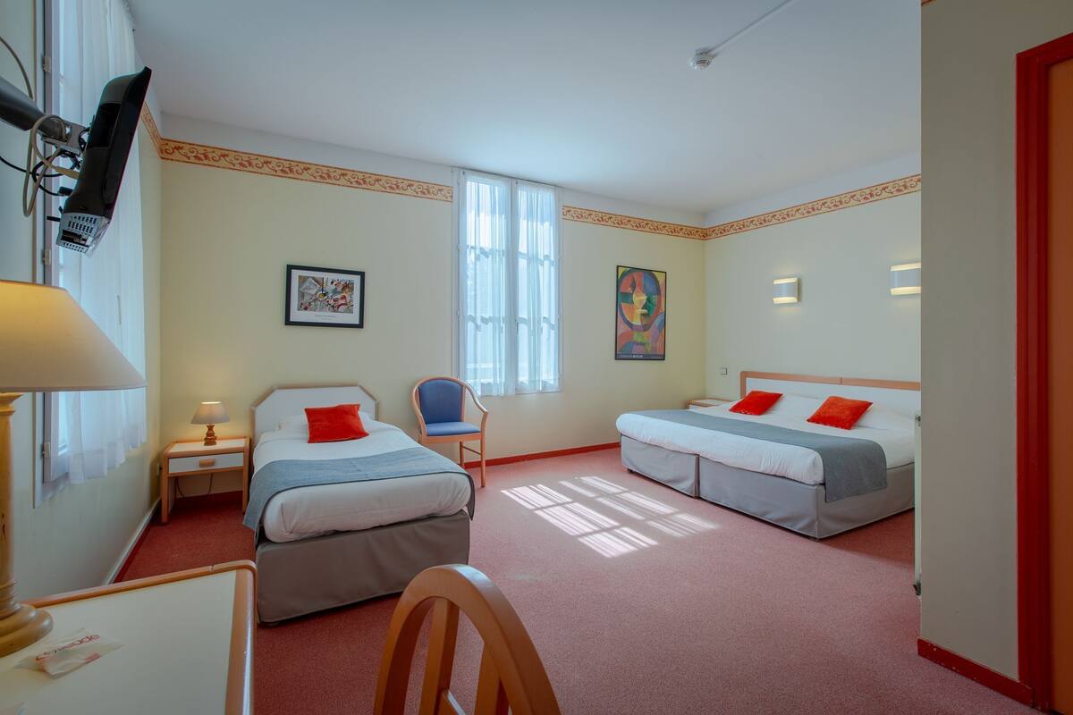 A hotel room with two beds, a chair, a desk, and a television.