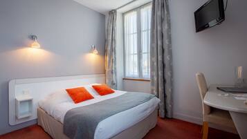 Habitación de hotel con cama, dos lámparas de noche, un escritorio, una silla, un televisor y una ventana con cortinas.