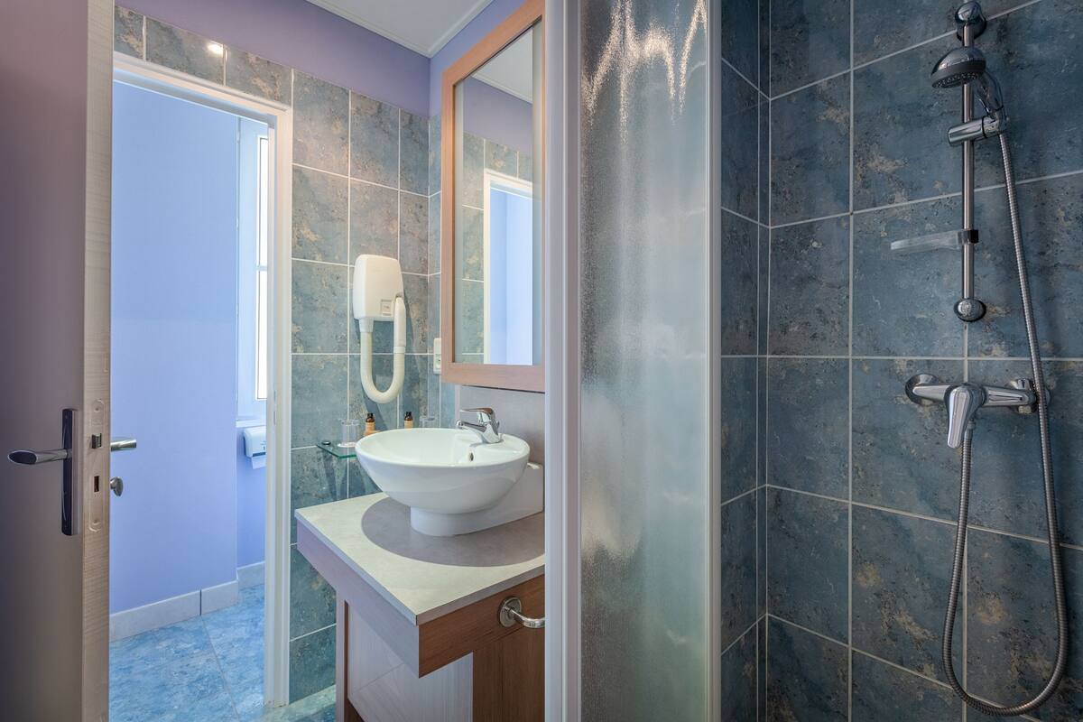 A modern bathroom with a white sink, a handheld showerhead, and a glass shower enclosure.