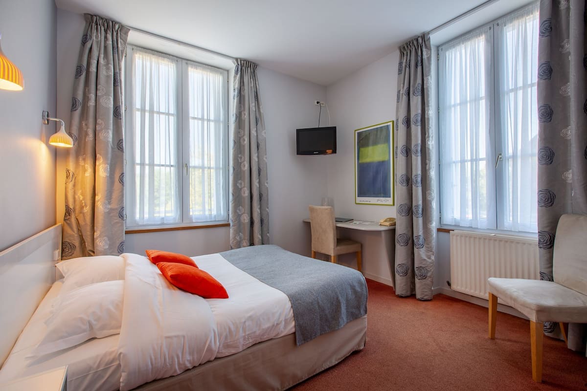 A hotel room with a bed, a desk, a chair, and a TV.