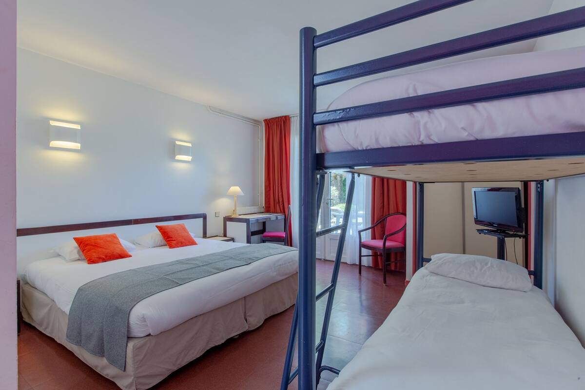 A hotel room with bunk beds, a desk with a chair, a TV, and a window with curtains.