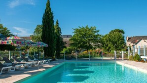 A swimming pool with lounge chairs and umbrellas, surrounded by trees and buildings. - Domaine de la Blairie (Gennes-Val-de-Loire)