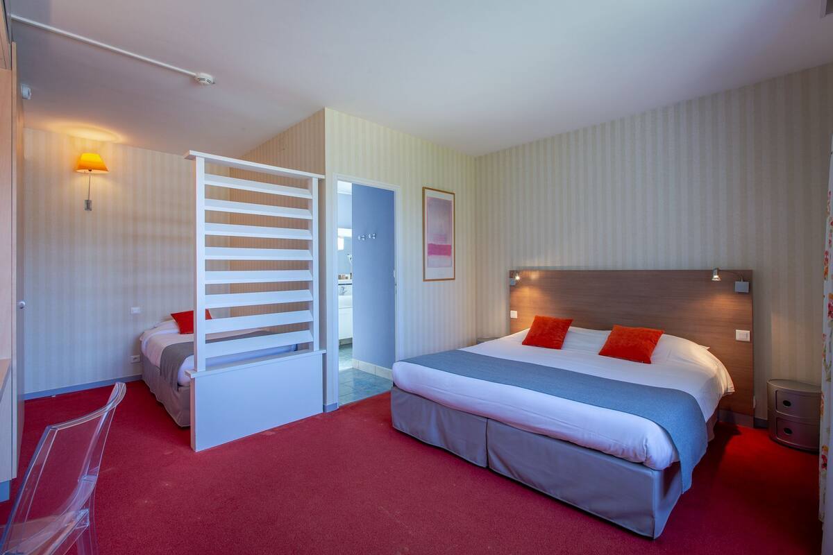 A hotel room with a bed, a desk, a chair, a wardrobe, and a door.