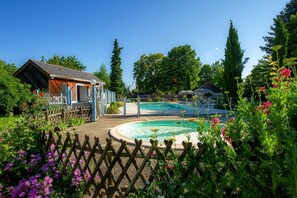 Una piscina rodeada por una valla de madera, con un pequeño edificio de madera y abundante vegetación al fondo.