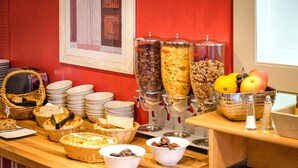 A buffet setup with various food items, including bread, cereal, and fruits, arranged on a wooden counter. - Domaine de la Blairie (Gennes-Val-de-Loire)
