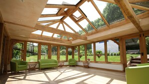 A spacious room with large windows, wooden beams, and green sofas. - Bickleigh Castle Hotel (Tiverton)