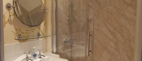 Un baño con ducha envuelta en vidrio, un lavabo blanco con espejo y un inodoro.