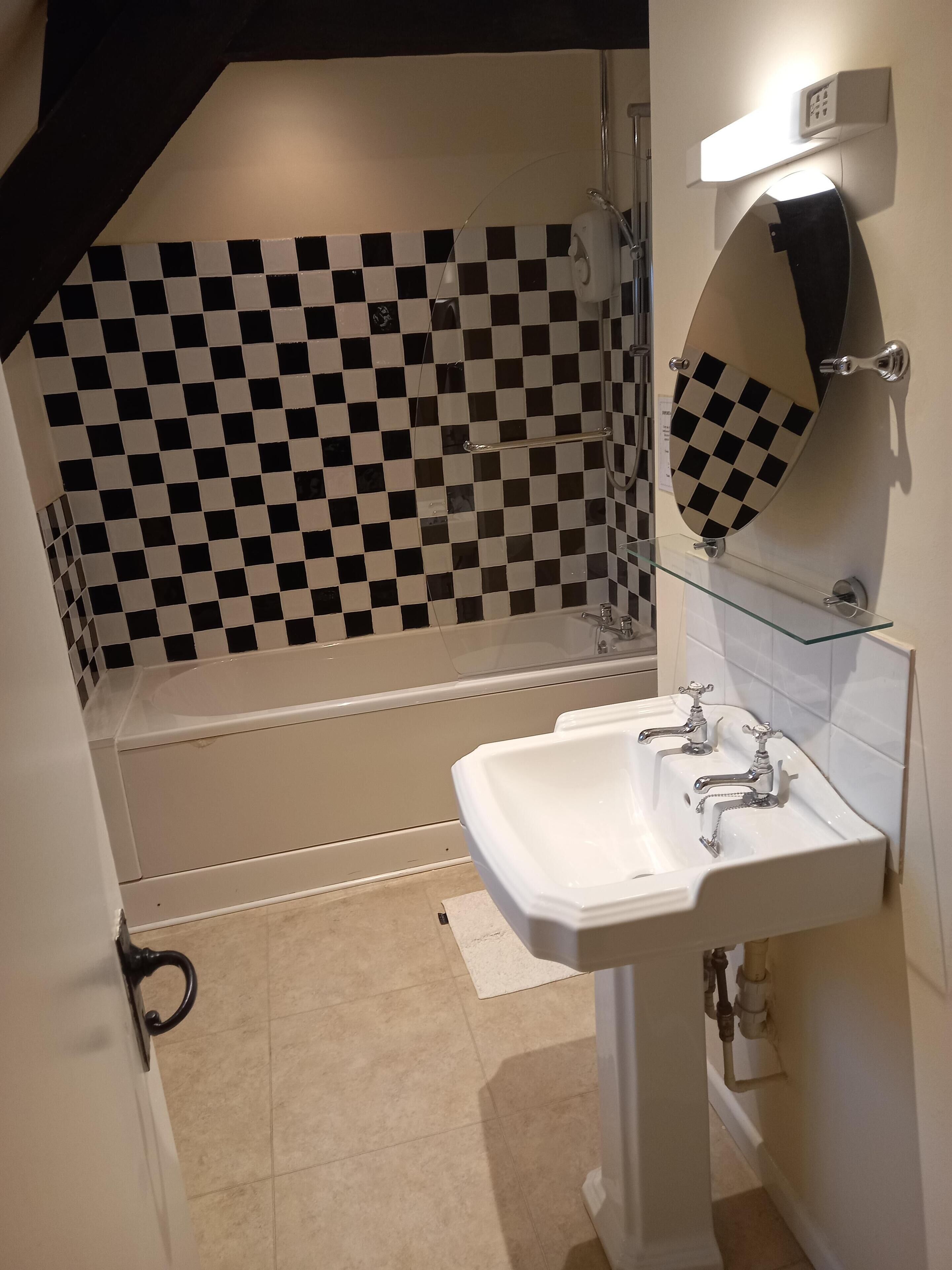 A bathroom with a checkered tile wall, a white bathtub, and a sink with two faucets.