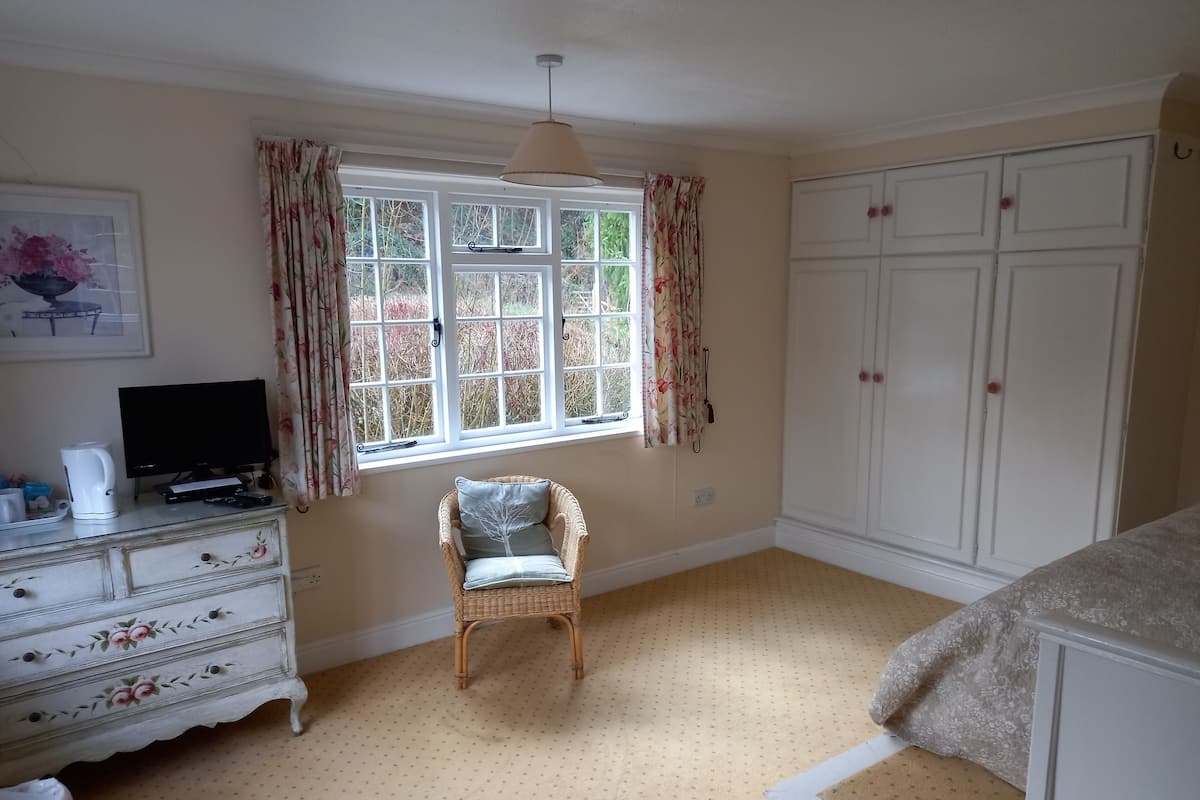 A bedroom with a bed, a dresser, a chair, a television, and a window with curtains.