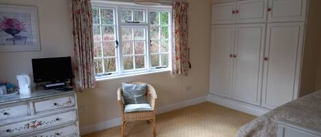 A bedroom with a bed, a dresser, a chair, a television, and a window with curtains.