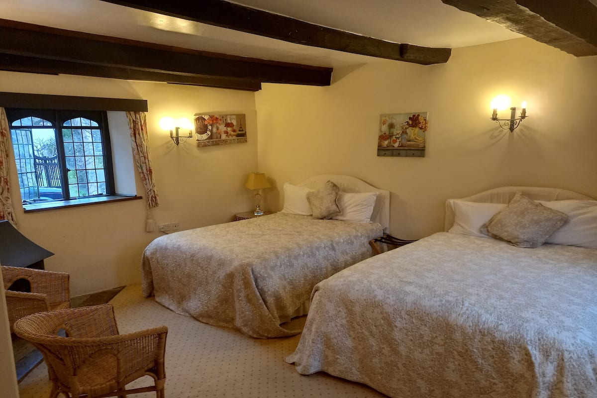 A room with two beds, a desk, and a chair. There are wall-mounted lamps and paintings.