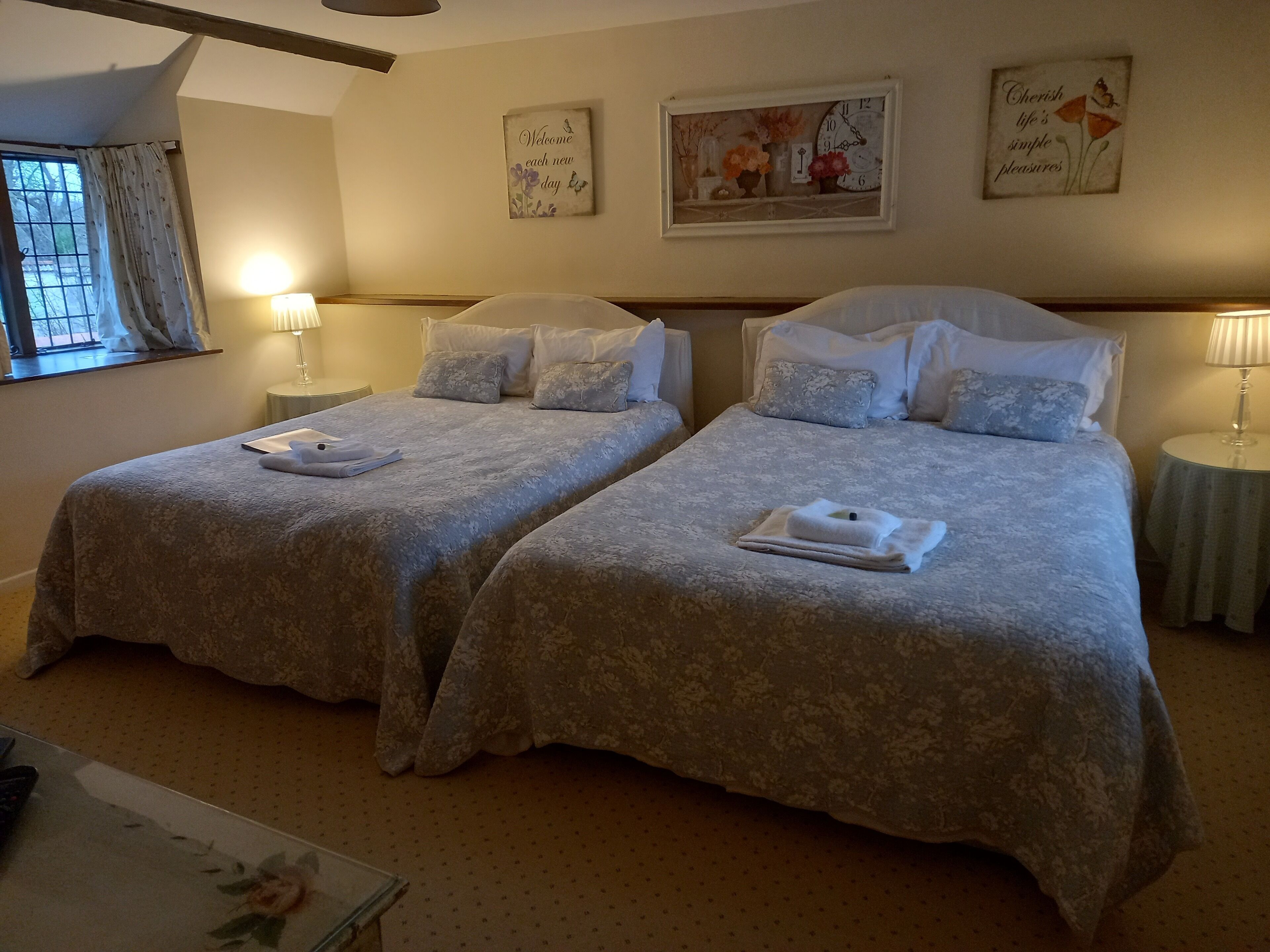 Una camera d'albergo con due letti, ciascuno con testiera e pediera abbinate, e un comodino con una lampada.