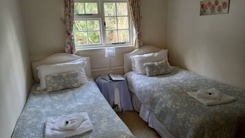 A room with two single beds, each with a pillow and a folded towel. There is a small table with a lamp between the beds.