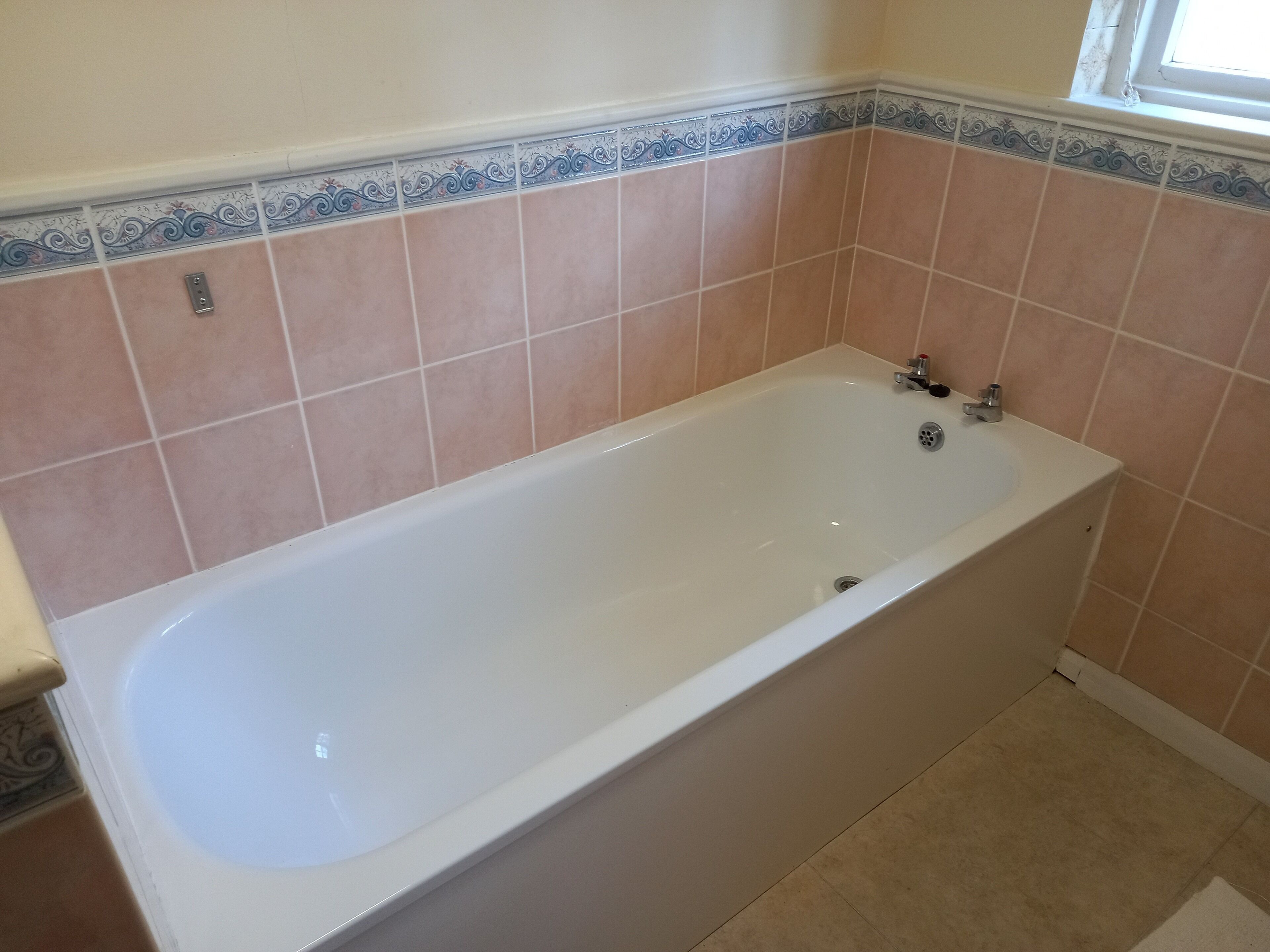 A standard rectangular bathtub with a faucet and drain, set against a wall with decorative tiles.