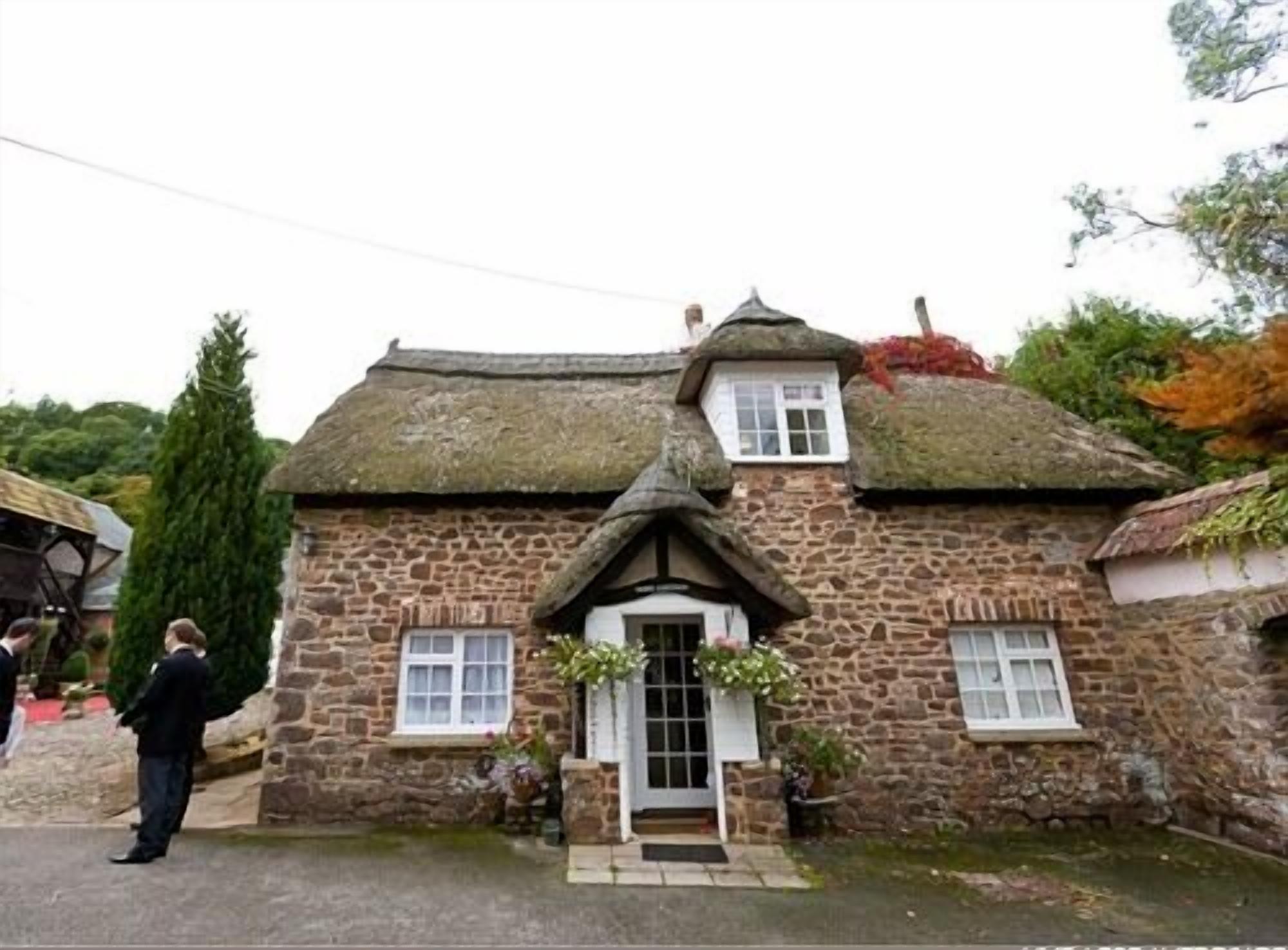 A stone cottage with a thatched roof, a small porch, and a window with a white frame.