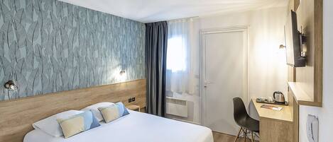 Habitación de hotel con cama, escritorio, silla, teléfono y ventana con cortinas.