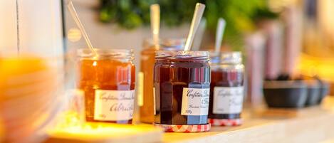 Three jars of honey with labels, placed on a wooden surface with a blurred background of greenery.