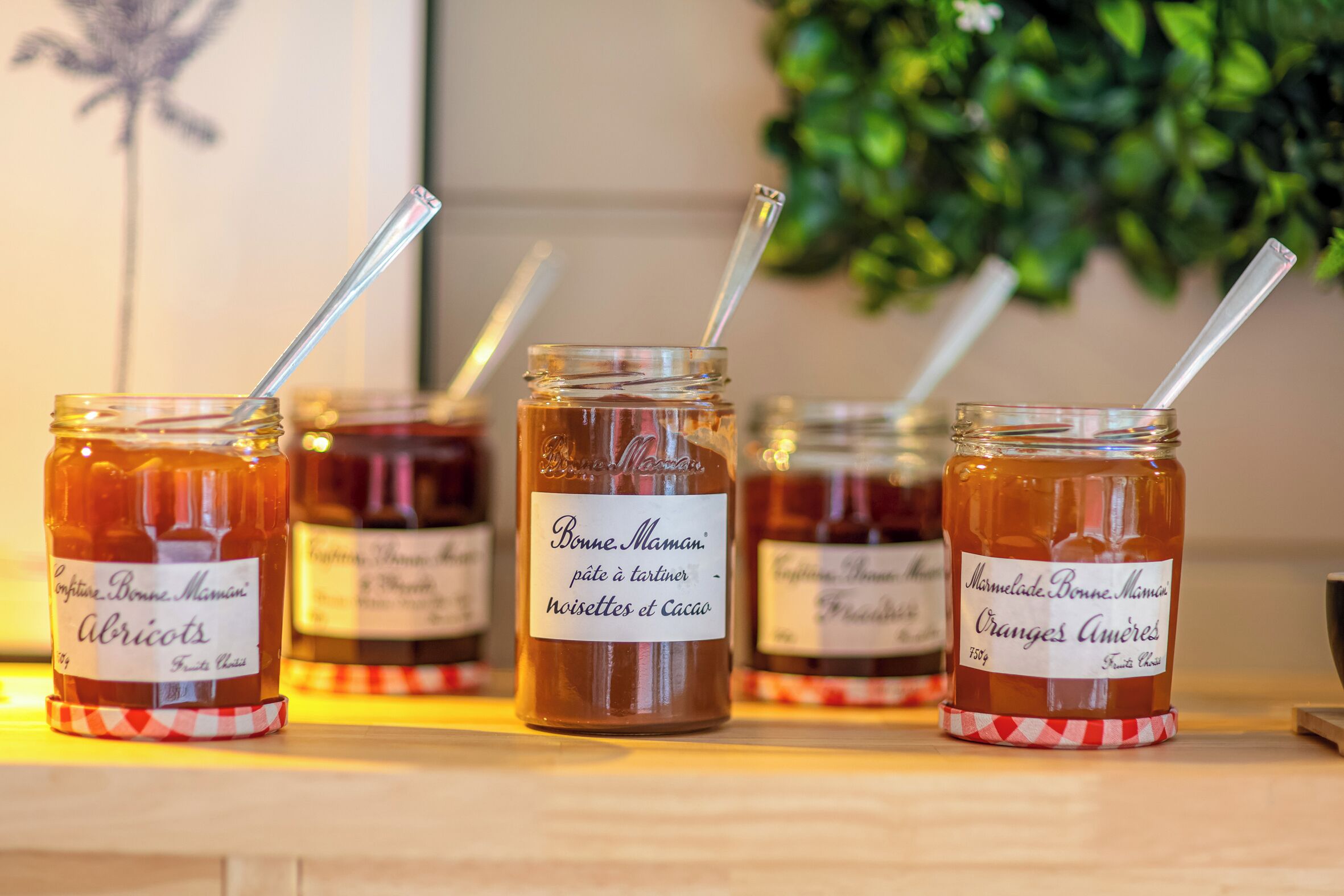 Four jars of honey with labels, each with a straw, on a wooden surface.