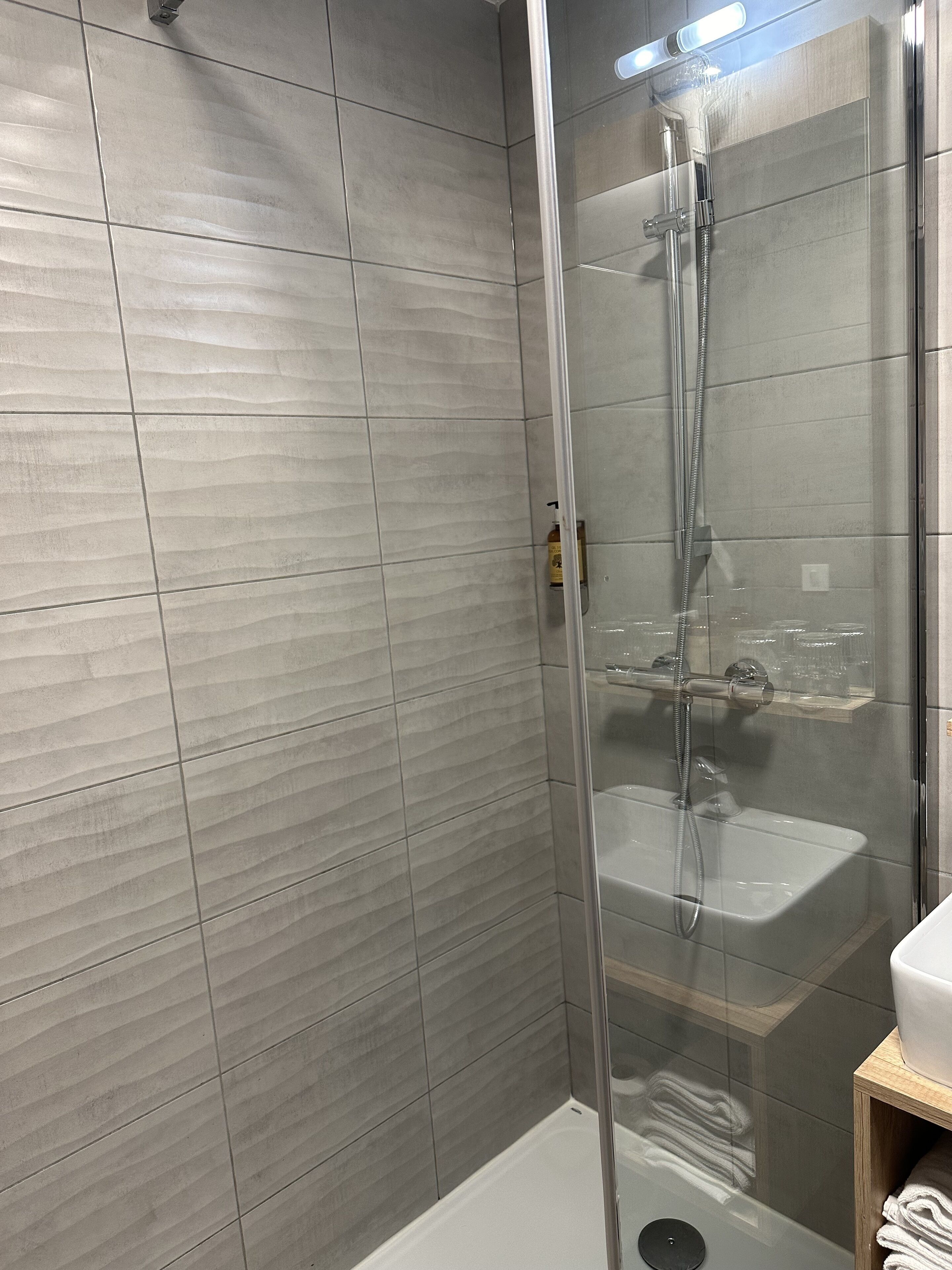 Een moderne douchecabine met een glazen deur, een handdouche en een ingebouwd wastafelmeubel.