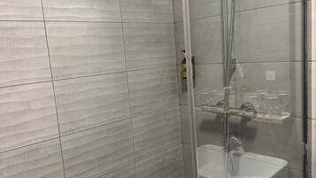 Een moderne douchecabine met een glazen deur, een handdouche en een ingebouwd wastafelmeubel.
