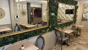 Ein Restaurant mit Spiegelwand, Holztischen, Korbstühlen und Fliesenboden.