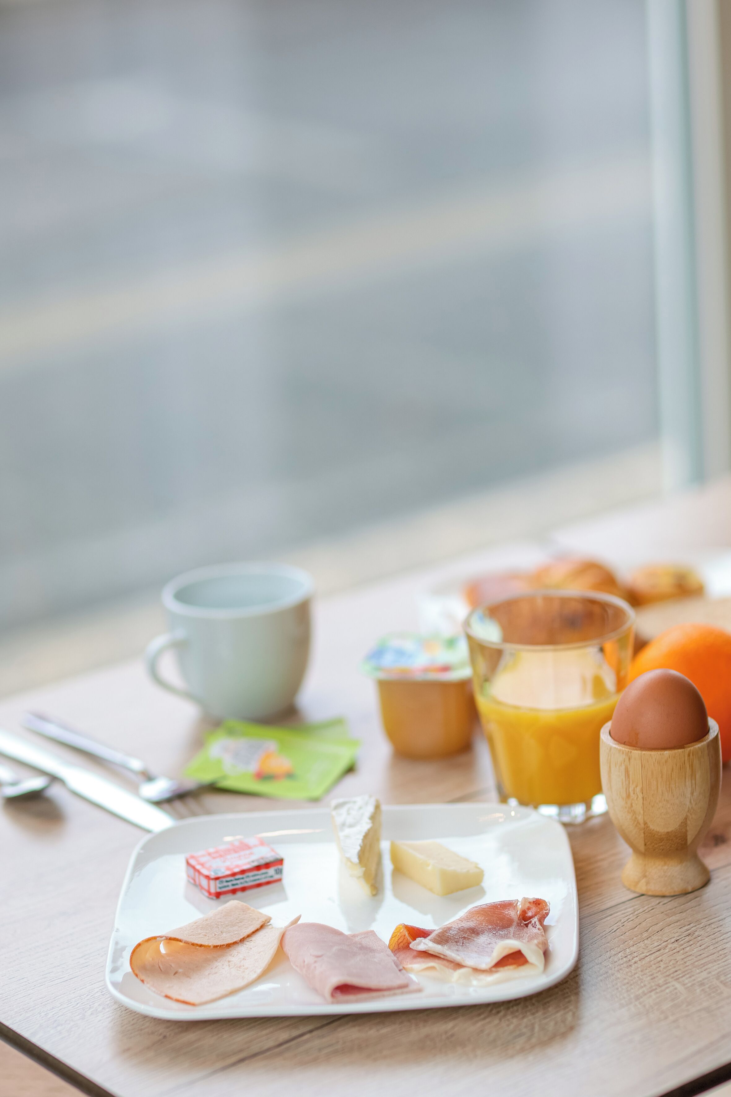 A breakfast tray with ham, cheese, and eggs on a plate, a cup, a glass of orange juice, and a wooden cup.