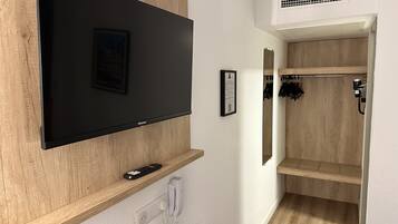 A modern hotel room with a mounted flat-screen TV, a telephone, and a mirror above a wooden shelf.