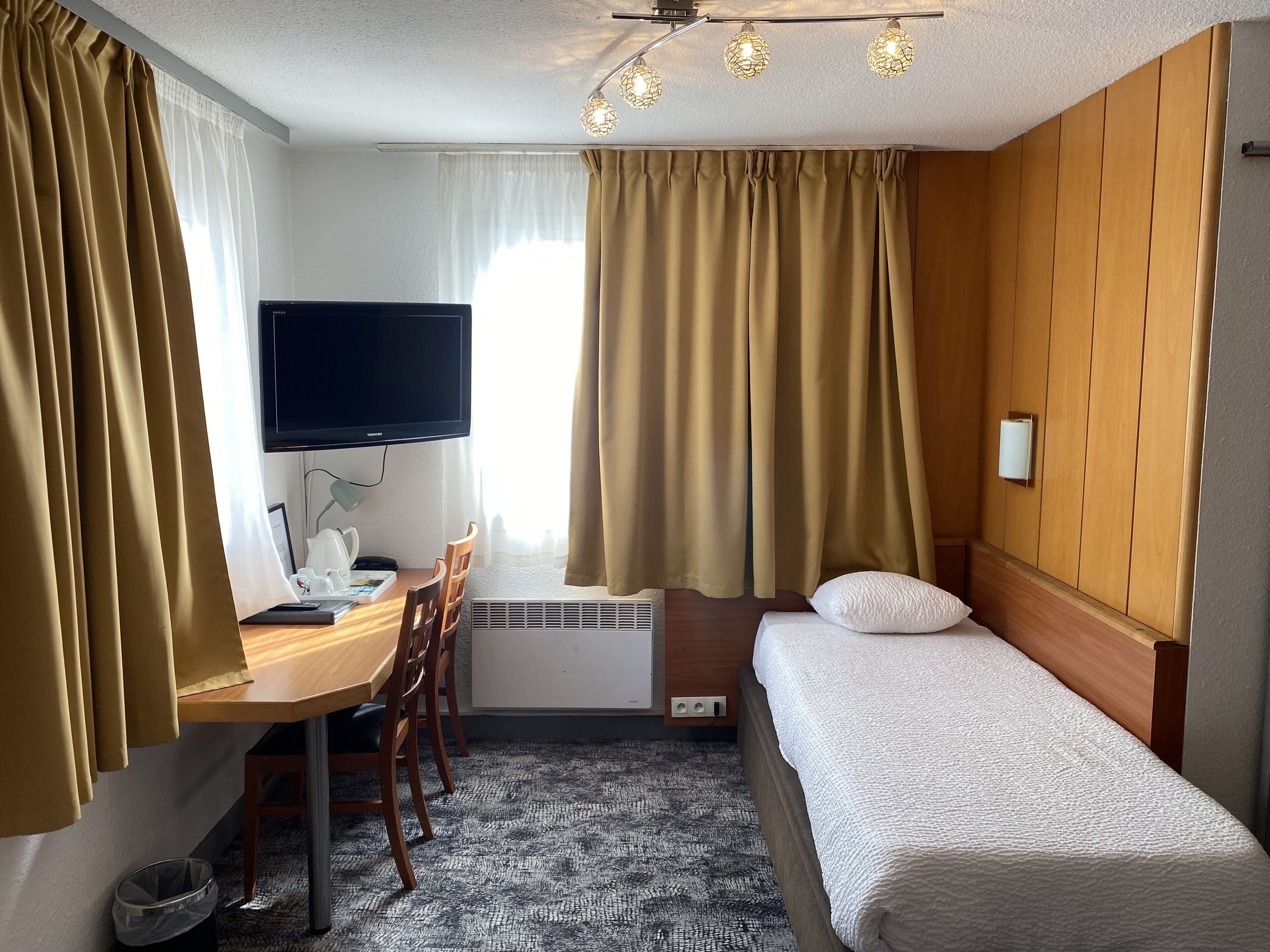 Une chambre d’hôtel avec un lit, un bureau et une chaise, une télévision et des rideaux.