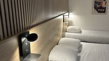A hotel room with a wooden slat wall, a bed with white linens, a wall-mounted light, and a framed picture of Pau.