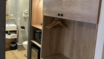 A compact bathroom with a shower, toilet, and sink. There is a wooden cabinet with a hanging rack and a small shelf.