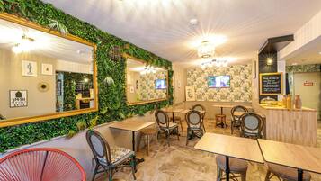 A restaurant with a green wall, multiple tables and chairs, and a mirror.