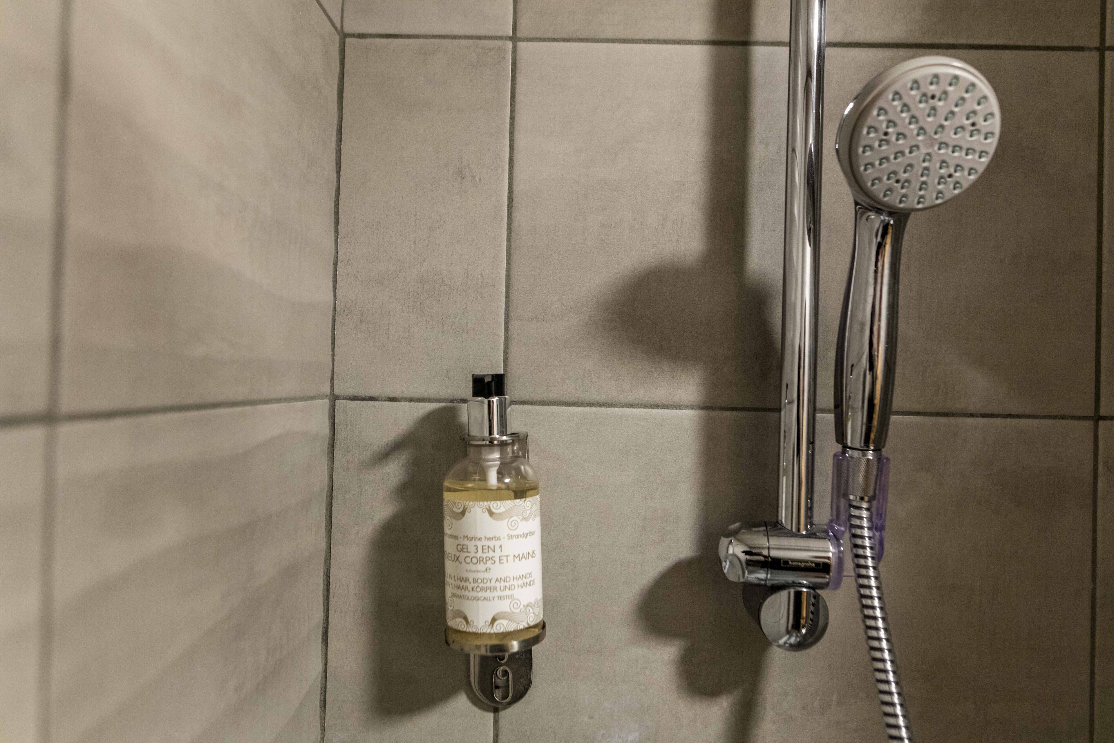 A bathroom with a shower, a handheld showerhead, and a bottle of shampoo.