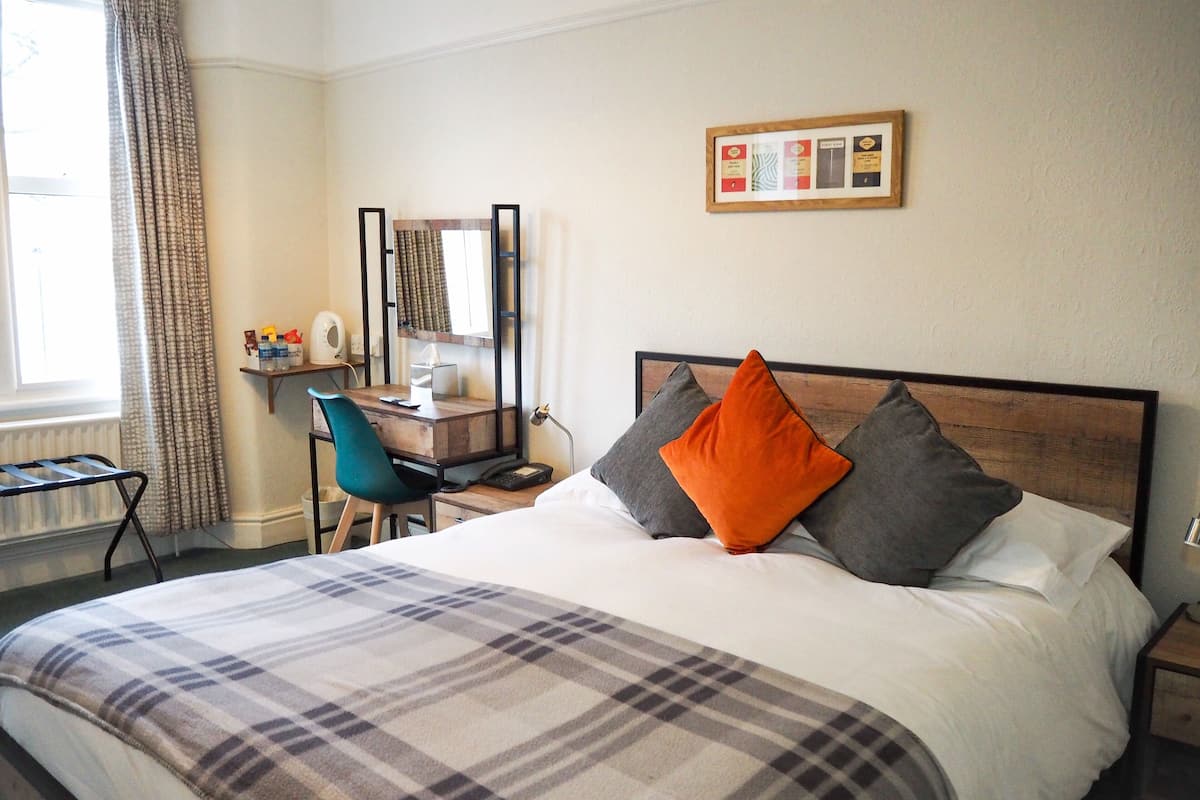 A hotel room with a bed, a desk, a chair, and a window with curtains.
