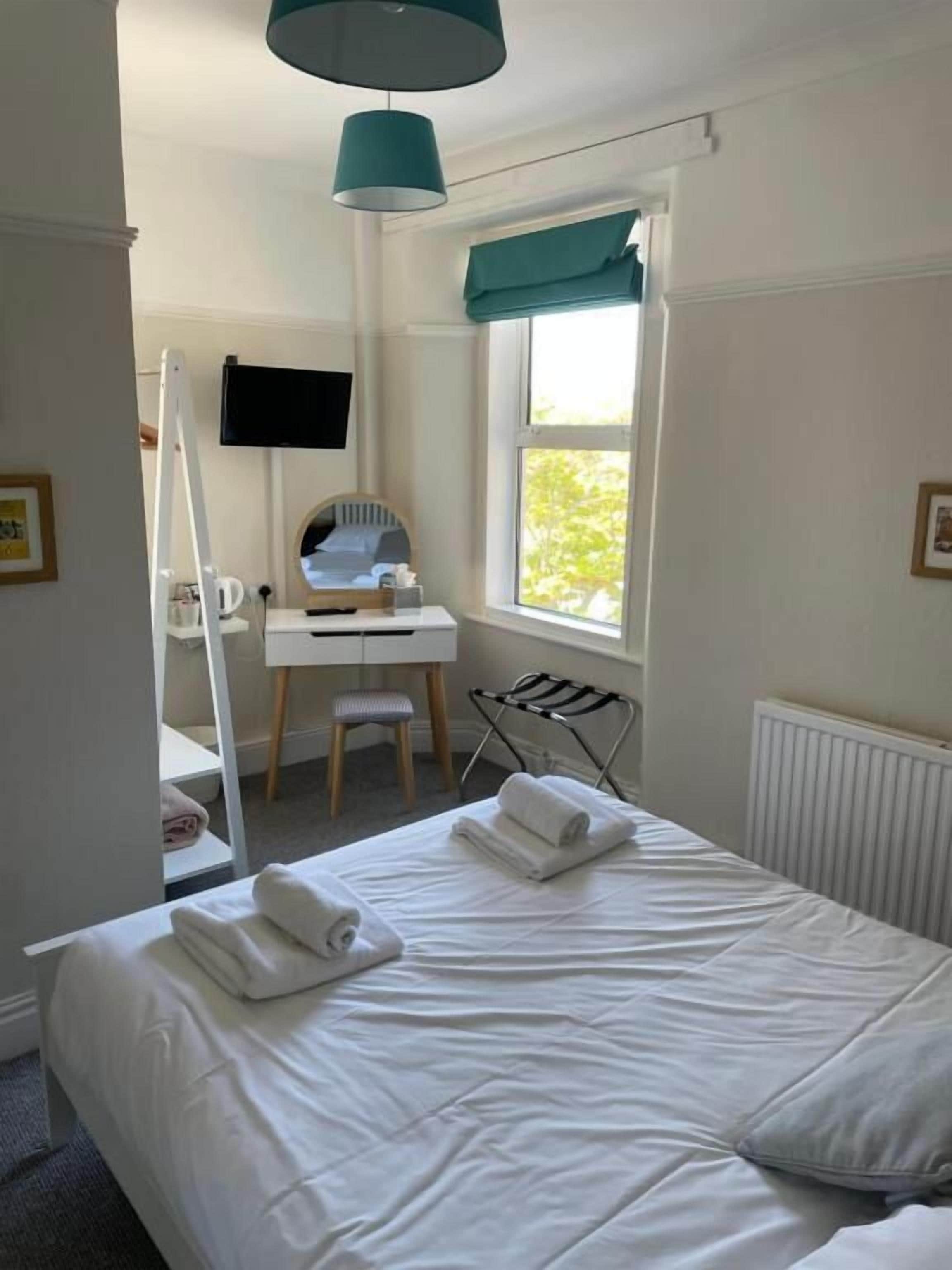 Habitación de hotel con cama, escritorio con silla, televisión montada en la pared y ventana con vista a la vegetación.