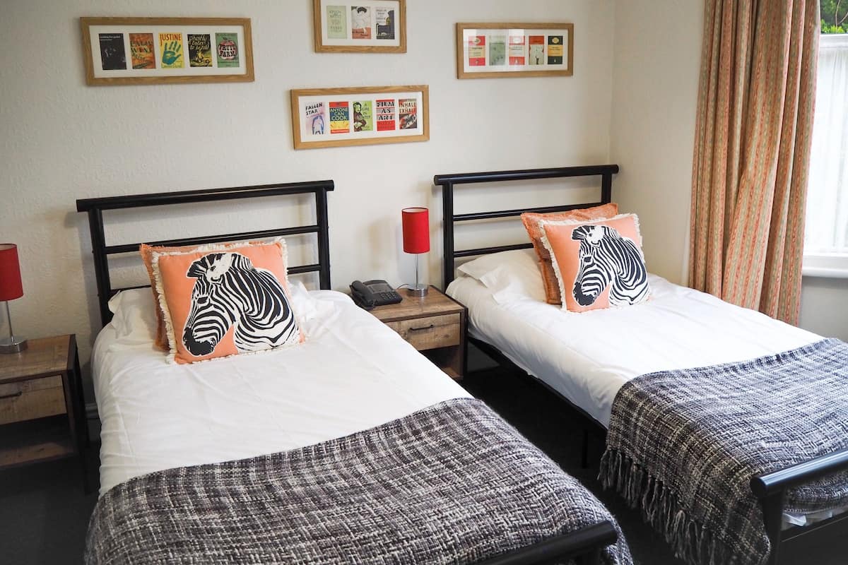 A hotel room with two beds, each with a zebra-themed pillow, a bedside table with a lamp, and framed pictures on the wall.