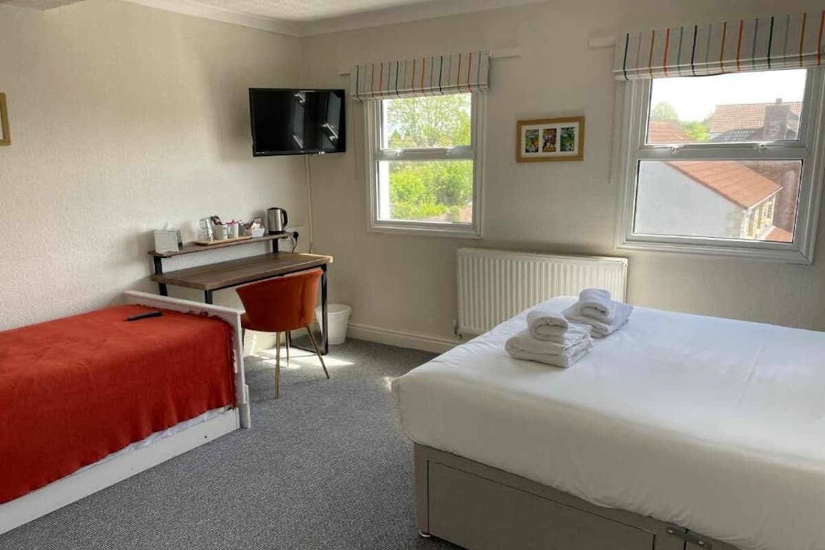 A hotel room with a bed, a desk, a chair, a television, and windows.