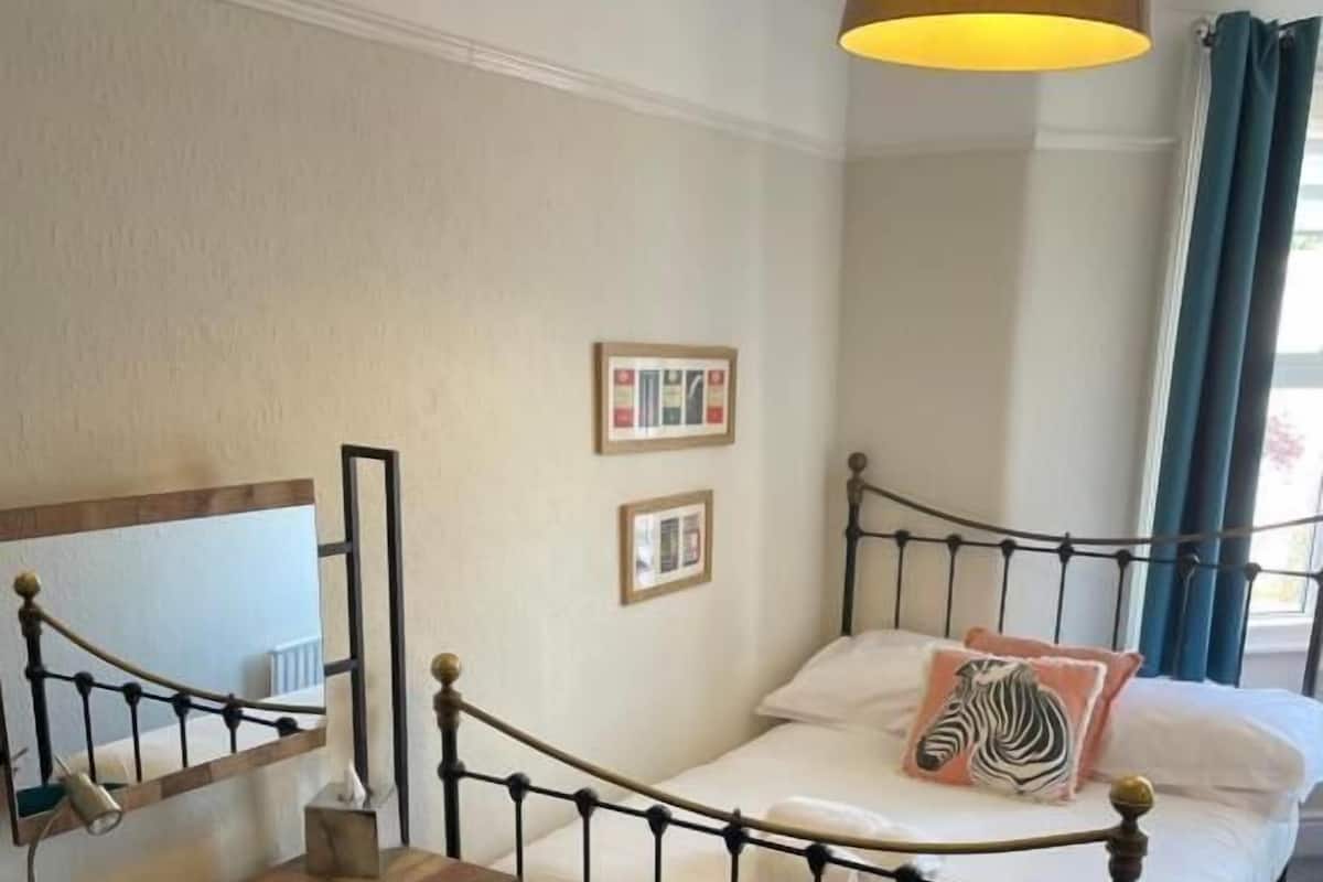 A bedroom with a bed, a desk, a chair, and a hanging lamp.