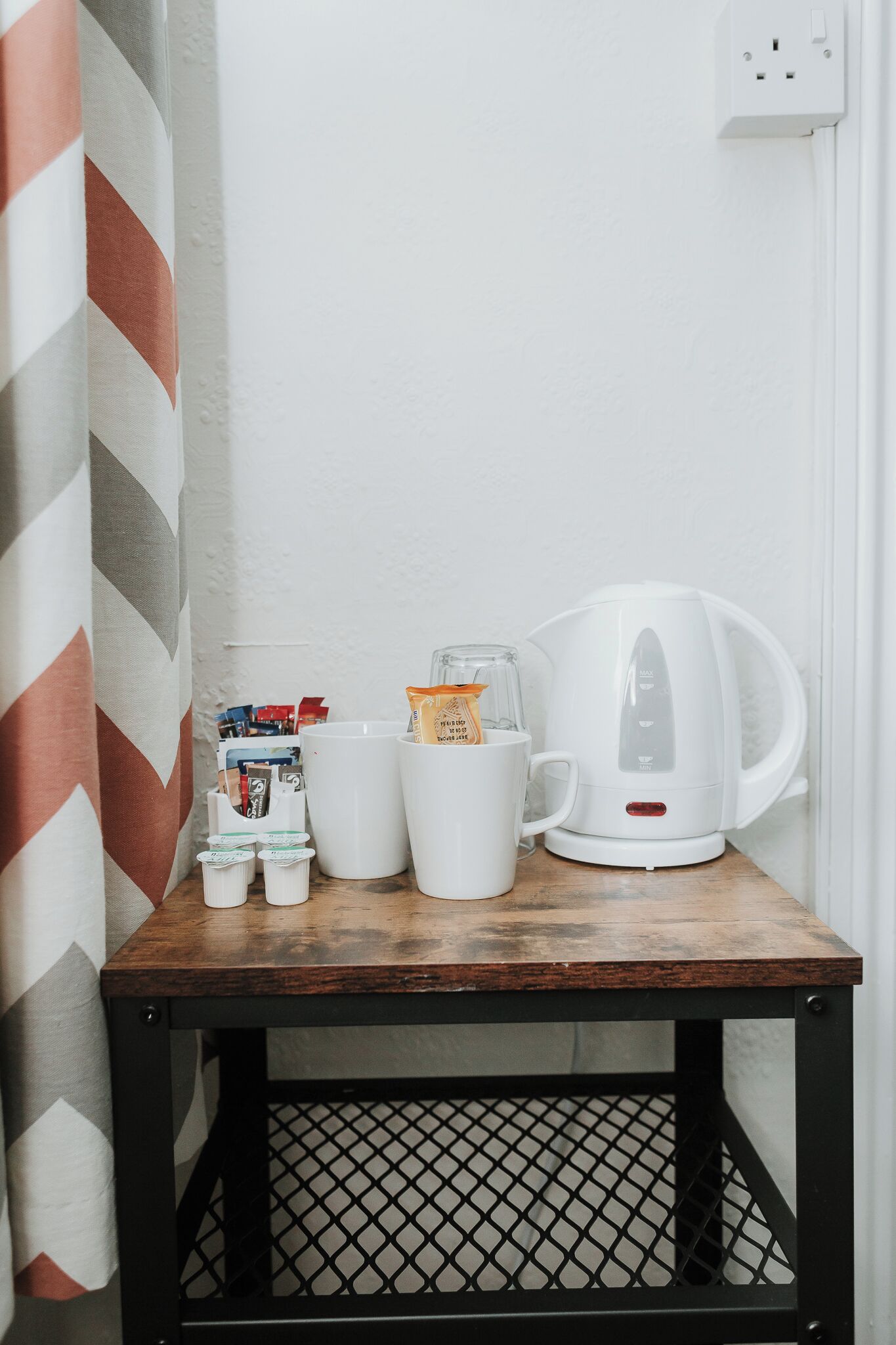 A small wooden table with a white kettle, two white mugs, and a glass container with a packet of tea.