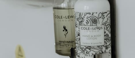 Two bottles of Cole & Lewis hand and body lotion mounted on a white tiled wall.