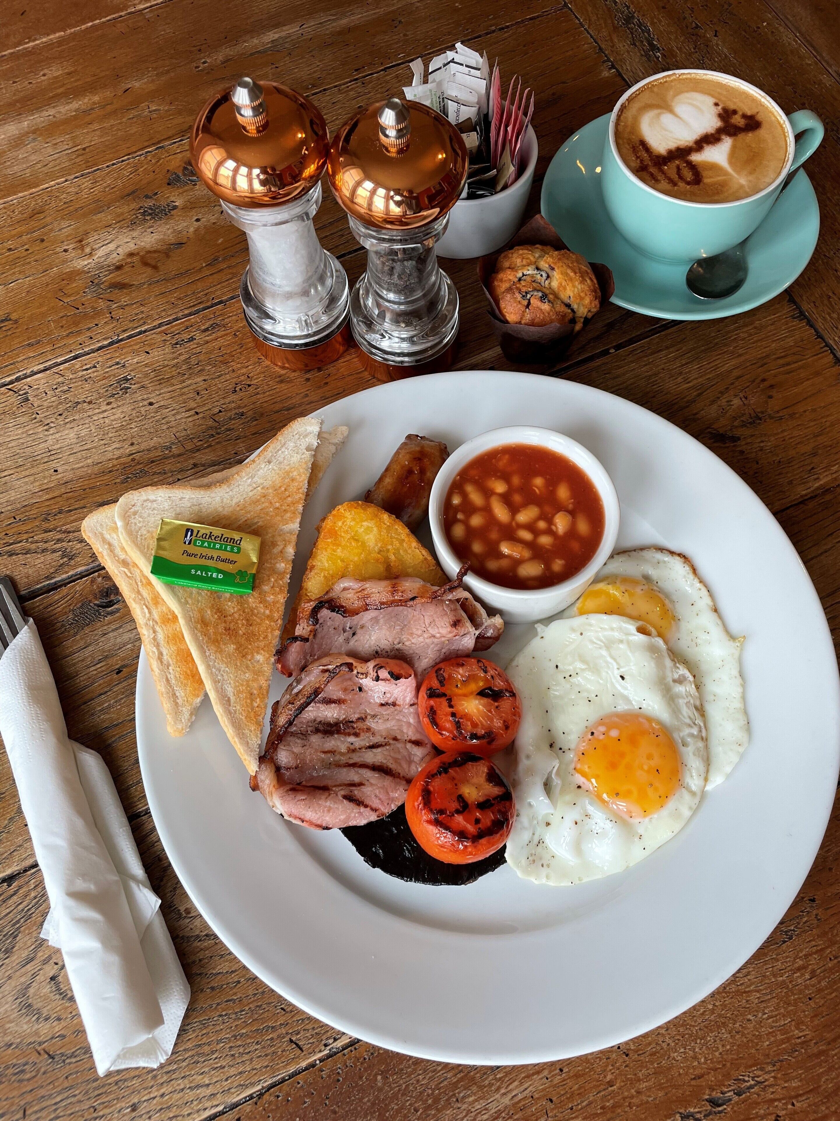 A breakfast plate with toast, beans, eggs, and bacon on a wooden table.