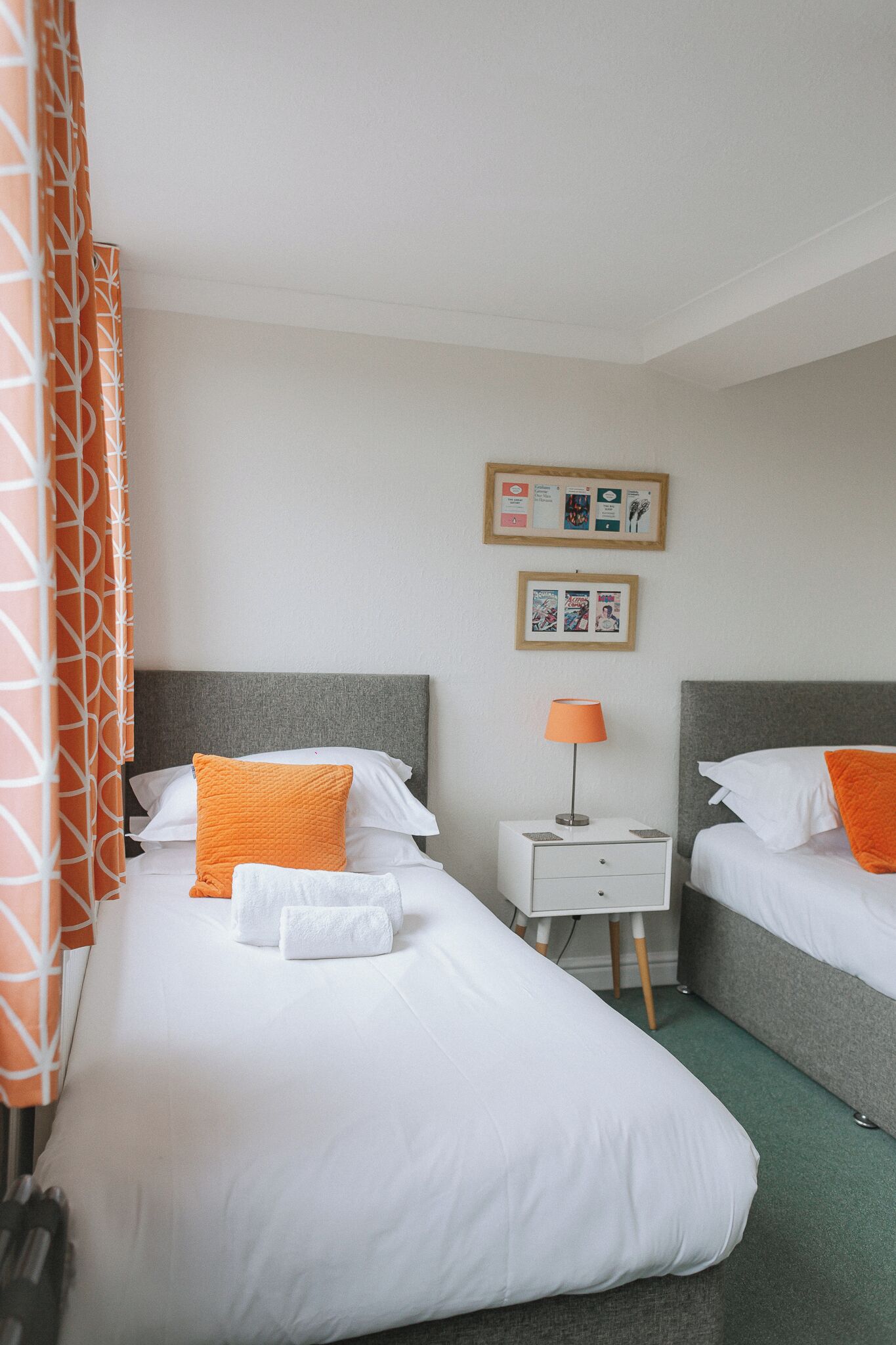 A hotel room with two beds, a nightstand, a lamp, and a bulletin board.