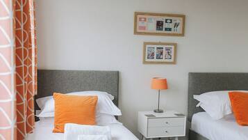 A hotel room with two beds, a nightstand, a lamp, and a bulletin board.
