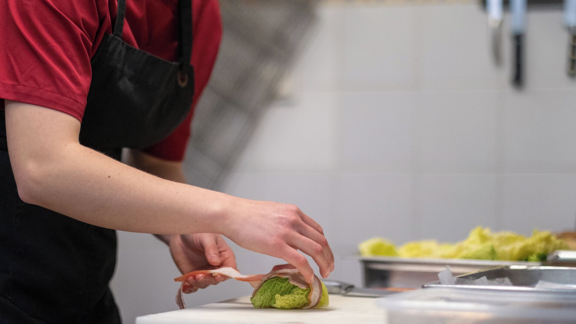 A person preparing food, specifically wrapping a green vegetable in bacon.